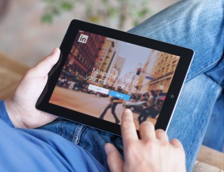 Personne consultant un profil LinkedIn sur une tablette, illustrant l’ajout d’un lien LinkedIn sur un CV pour une recherche d’emploi.